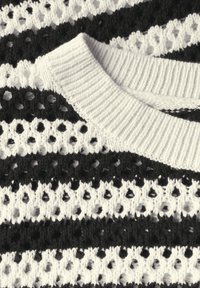 Gestreifter Strickstoff in Schwarz und Weiß mit Lochmuster. Rippkragen in Weiß. Texturierte Oberfläche mit abwechselnd festen und Spitzenabschnitten.