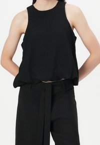 Mustat hihattomat paita, jossa on tekstuuri, pyöreä pääntie ja löysä istuvuus, yhdistettynä samaan sarjaan korkeavyötäröisiin housuihin, joissa on solmimisvyötärö.