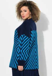 Pull oversized en mélange de laine avec de vives motifs en zigzag bleu et marine, des poignets côtelés et une finition légèrement texturée.