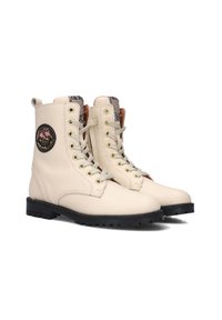 Crèmekleurige leren veterschoenen met een gestructureerde afwerking, gouden hardware en een ronde patch met bloemmotieven aan de zijkanten. Zwarte rubberen zool.