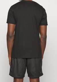 Sort bomulds t-shirt med korte ærmer, rund halsudskæring og en glat tekstur. Båret med sorte mesh-shorts med sidelommer.