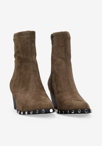 Botas de tobillo de ante marrón con punta afilada, cierre de cremallera y tacón negro. Estrellas de plata adornan la parte delantera y el borde de la suela.