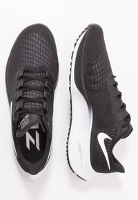 Baskets de sport noires avec une tige texturée, présentant un logo swoosh blanc, des lacets et une semelle rembourrée avec un motif de semelle distinct.