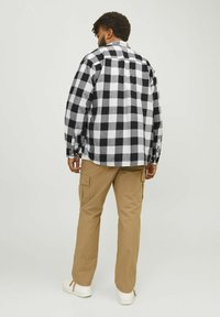 Camisa de franela a cuadros en blanco y negro con mangas largas, combinada con pantalones cargo en color beige y zapatillas blancas. Diseño visible en la parte de atrás y en los puños.