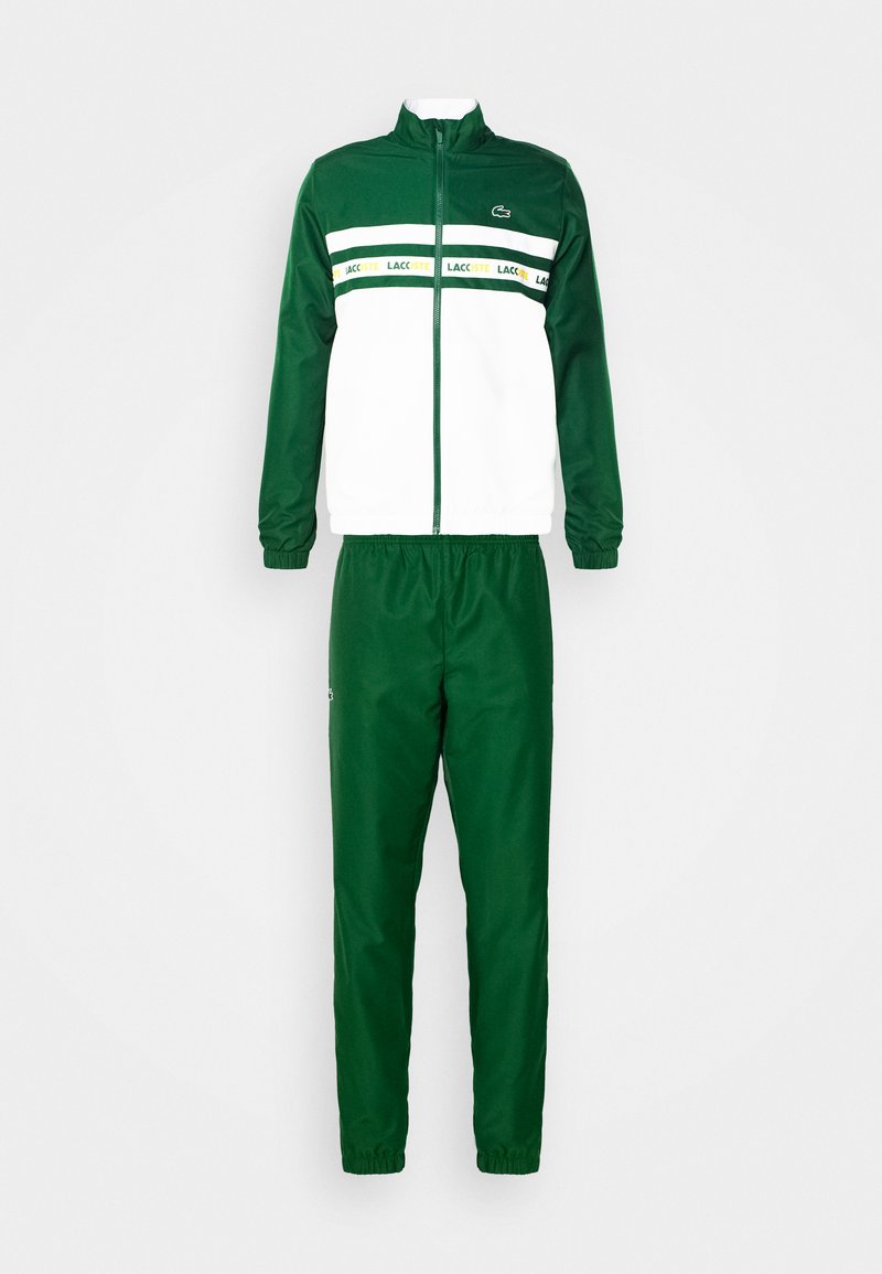 Ensemble de survêtement vert et blanc en tissu synthétique lisse. La veste possède une fermeture éclair à l'avant, un col haut et des rayures horizontales colorées.