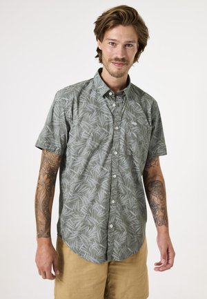 Camisa de botón de manga corta en verde oliva con un ligero estampado de hojas. Presenta un bolsillo en el pecho y detalles de botones blancos.