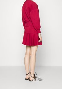 Czerwony skrócony sweatshirt z pełnymi rękawami, zestawiony z rozkloszowaną spódnicą. Obuwie ma zdobienia z koralików oraz wiązania wokół kostek.