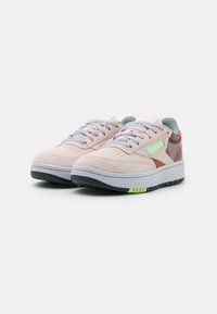 Beiga mockasonskor med grå snören, gröna och röda detaljer, samt en vit mellansula med en svart och grönrandig yttersula.