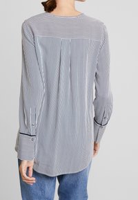 Camicia a maniche lunghe a righe con yoke posteriore, orlo arrotondato e polsini a contrasto. Realizzata in tessuto leggero nei colori blu navy e bianco.