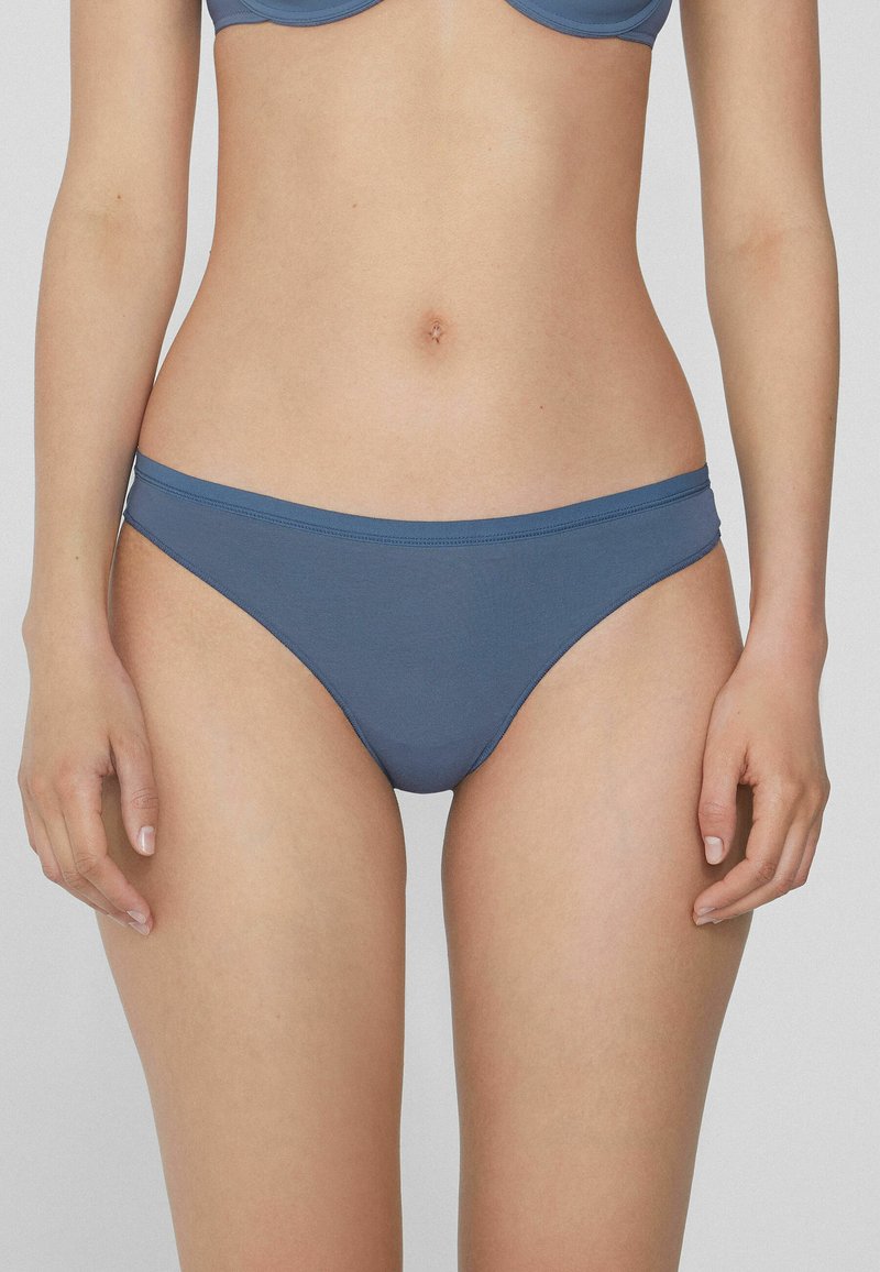 Blaue Unterwäsche aus einem glatten, dehnbaren Stoff, mit tiefem Schnitt und minimalistischem Bündchen. Sie hat einen nahtlosen Abschluss für zusätzlichen Komfort.