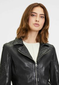 Zwarte leren motorjack met studs op de schouders, ritssluiting en een kraag met inkeping; gladde textuur en getailleerd ontwerp.