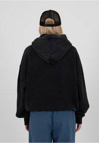 Hoodie noir surdimensionné avec capuche à cordon, texture douce et épaules tombantes. Pantalon bleu visible en bas.