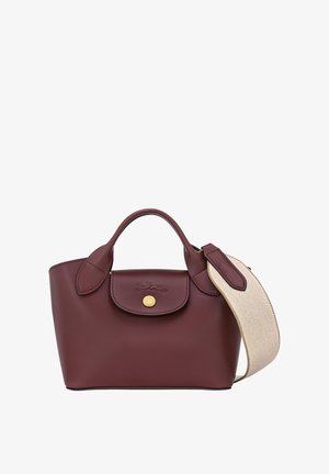 Burgundy leather handbag featuring a rounded shape, dual handles, and a textured cream strap. Gold hardware accents complete the design.