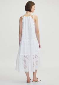 Vestido largo sin mangas blanco con patrón de encaje floral y diseño en capas. Las tiras ajustables y el dobladillo con forma de ola acentúan la silueta fluida.