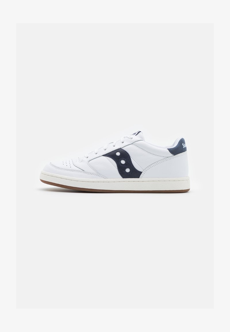 Zapatilla de cuero blanco con detalles en azul marino, diseño de cordones y lados perforados. Presenta una suela de goma blanca y un logotipo azul oscuro en contraste.