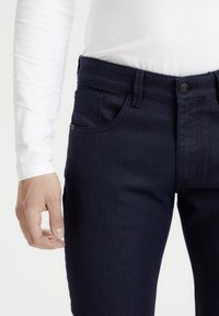 Vaqueros de mezclilla azul oscuro con corte ajustado, que cuentan con bolsillos frontales, costuras contrastadas y una cinturilla con cierre de botón.