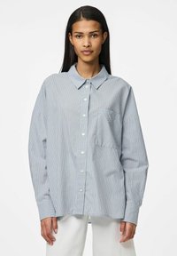 Plava i bijela prugasta košulja s dugim rukavima, s dugmadi sprijeda, ovratnikom i jednim džepom na prsima. Mekani materijal s opuštenim krojem.