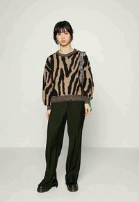 Pulôver de tricô listrado em castanho e preto com mangas balão, combinado com calças largas pretas com pregas. Acentuado com uma alça no ombro.