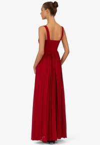 Rotes Maxikleid mit breiten Trägern, einem gerafften Oberteil und einem schwingenden, gefältelten Rock. Der Stoff wirkt leicht und hat eine glatte Textur.