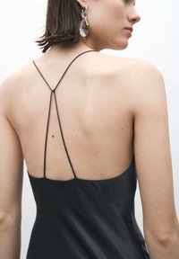 Vestido negro sin mangas con finas tiras cruzadas, tejido suave y diseño de espalda baja, con costuras mínimas y un ligero brillo.