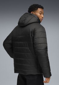 Giacca imbottita nera con cappuccio, design a baffle orizzontale e texture liscia. Il modello è visto da dietro, mettendo in mostra la vestibilità del capo.