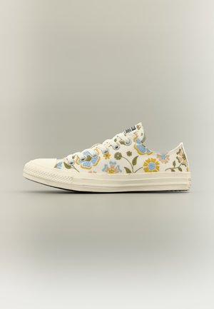 Witte lage sneaker met canvas bovenzijde, versierd met blauw, geel en groen bloemenborduursel, en een witte rubberen zool en veters.
