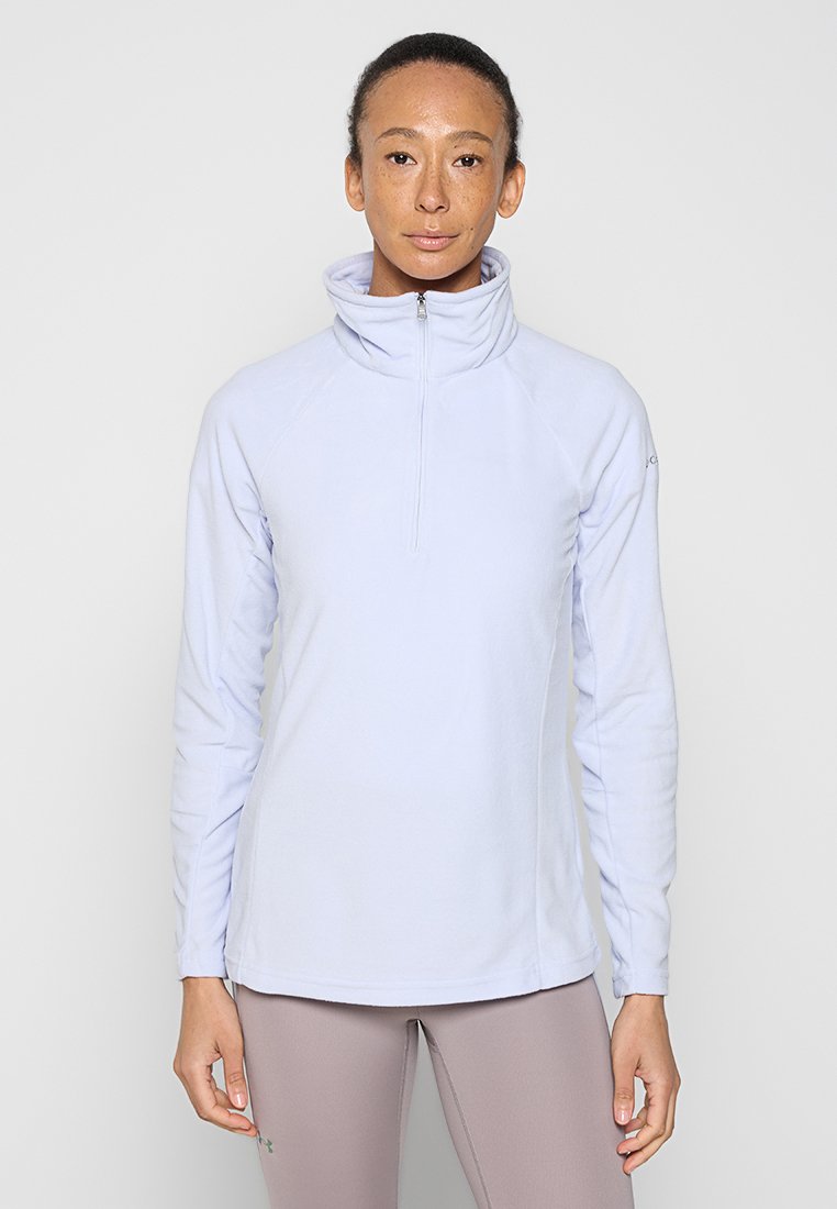 Fleece de cremoso morado claro con cierre, cuello alto, mangas largas y costuras raglán, que presenta una textura suave y un diseño ajustado.