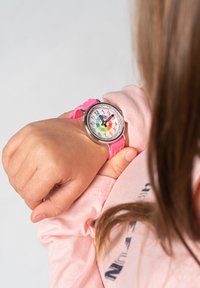 Montre ronde avec un cadran coloré présentant de grands chiffres sur une lunette en métal argenté. Bracelet en silicone rose vif et des repères horaires multicolores éclatants.