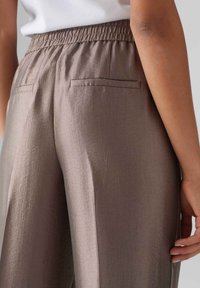 Bruine textuur wijde broek met een elastische tailleband, voorzien van twee achterzakken en soepel, vloeiend materiaal.