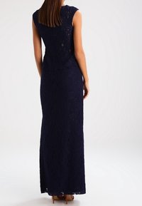 Robe en dentelle bleu marine avec un corsage moulant et une jupe longue et fluide. Elle présente un design sans manches et un ourlet festonné.