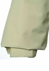 Valkoinen beige housunlahje, jossa on tarrasolki kiinnitettynä lahkeen reunaan, näyttäen kankaan tekstuurin ja ommellut reunat.