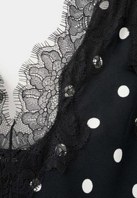 Czarna tkanina w białe kropki, obszyta delikatną czarną koronką kwiatową z cienką siateczką i misternymi detalami.