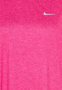 Vaaleanpunainen urheilupaita, joka on valmistettu teksturoidusta, kosteutta siirtävästä kankaasta. Paitassa on pieni valkoinen Nike-logo kaulan lähellä.