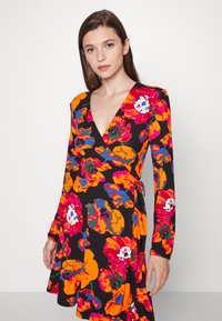 Vestido estampado com flores, apresentando padrões vibrantes em laranja, rosa e azul sobre um fundo preto, mangas longas e decote em V.