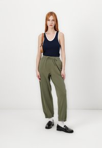 Marineblå tanktop med hvid kant, olivengrøn bukser med snore, sorte loafers og hvide sokker, båret med en brun skuldertaske.