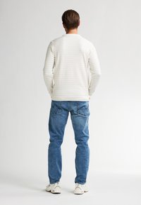 Witte, gestructureerde lange mouwen shirt met horizontale strepen, gecombineerd met blauwe jeans. Model gezien vanuit de rug, met lichte sneakers.