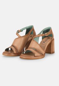 Tan leather block-heeled sandals with cross-strap design, open-toe, and adjustable ankle buckle. Interior features light blue lining.