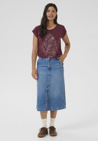 Un t-shirt bordeaux à manches courtes avec une impression détaillée, associé à une jupe maxi en denim bleu et des chaussures à lacets marron avec des chaussettes beiges.