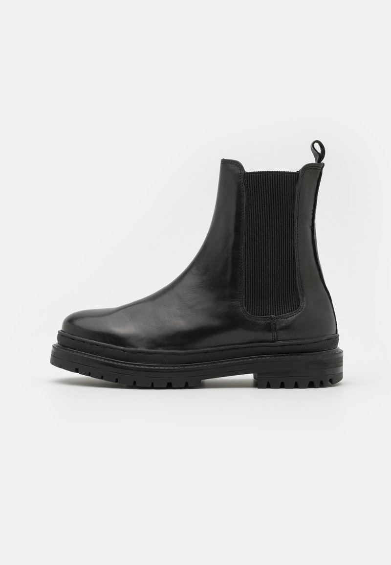 Botte Chelsea en cuir noir avec panneau latéral élastique, languette à l’arrière et semelle épaisse crantée, vue de profil sur fond blanc.