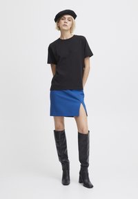 Svart bomulls-t-shirt, blå mini-kjol med sidöppning och knähöga svarta läderstövlar. En beret som accent fulländar looken.