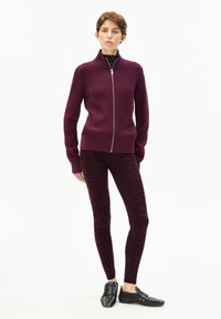 Burgunderfarbener, gerippter Reißverschluss-Pullover, kombiniert mit dunkelburgunderfarbenen Leggings mit Zebramuster und schwarzen Slippern mit silbernen Nieten.