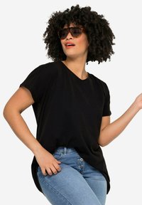 Czarny t-shirt z krótkim rękawem i dekoltem w serek, noszony z jasnoniebieskimi dżinsami o wysokim stanie. Modelka ma kręcone włosy i nosi okulary przeciwsłoneczne.