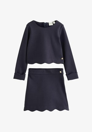 Top cropped cu mâneci lungi, bleumarin și fustă asortată cu tivuri ondulate și nasturi mici metalici cu logo pe fiecare piesă.