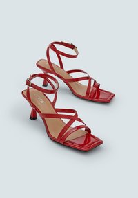 Rode gepatineerde leren sandalen met hak, vierkante neus, meerdere gekruiste banden en een zwarte accenthak. Glad oppervlak en glanzende afwerking.