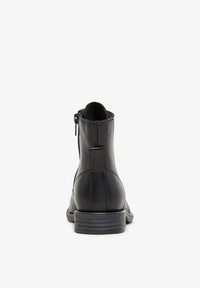 Bottines en cuir noir avec une finition lisse, fermeture éclair sur le côté et un petit talon empilé. Elles présentent une semelle texturée et de simples accents de coutures.