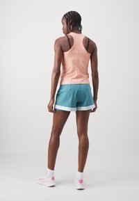 Őszibarack színű tank top, racerback fazonnal, türkiz színű sorttal, fehér díszítéssel párosítva. A modellen fehér cipő és zokni van.