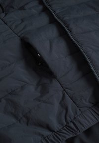 Quilted dark navy jacket featuring a zip closure, smooth texture, elastic waist, and side pocket openings.