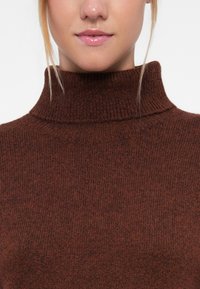 Bruine geribde turtleneck trui gemaakt van textuur gebreid materiaal, met een hoge hals en een nauwsluitend ontwerp.