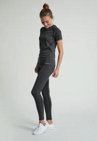 Mørkegrå atletisk skjorte med teksturerede skuldre og mønstrede sider, parret med matchende leggings med et chevronmønster. Hvide sneakers fuldender looket.