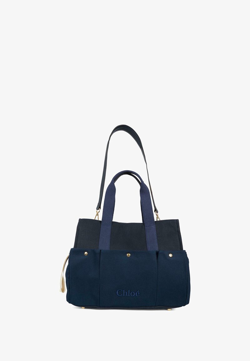 Granatowa torba płócienna z podwójnymi uchwytami, złotymi akcentami i wytłoczonym logo. Posiada usztywniony kształt oraz kontrastowe sekcje materiału.